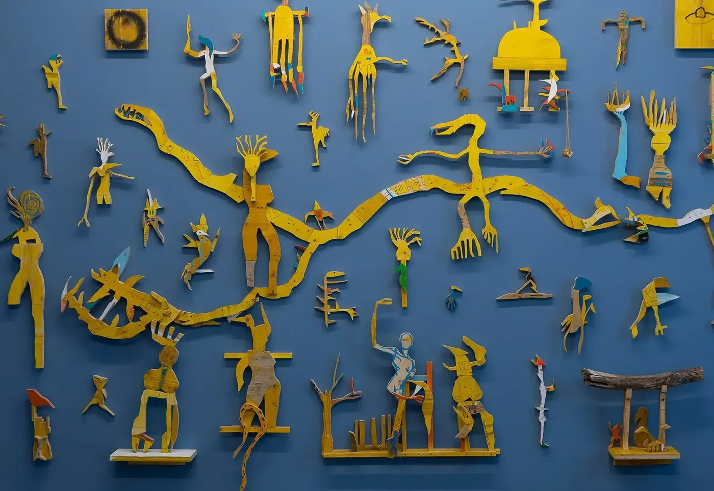 Wide wall installation of yellow wood cutout figures by Ernst Koslitsch, Beings & Creatures, rotor, Graz