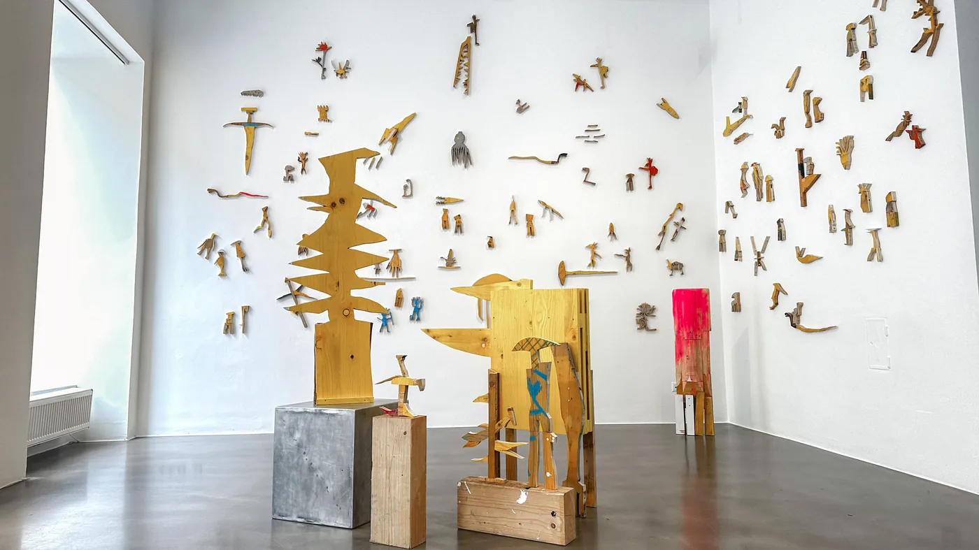 Wall constellation of dozens of small painted wood fragments with two freestanding yellow totem sculptures on plinths, Cosmic Trigger – Respawn, Bildraum 07, Ernst Koslitsch