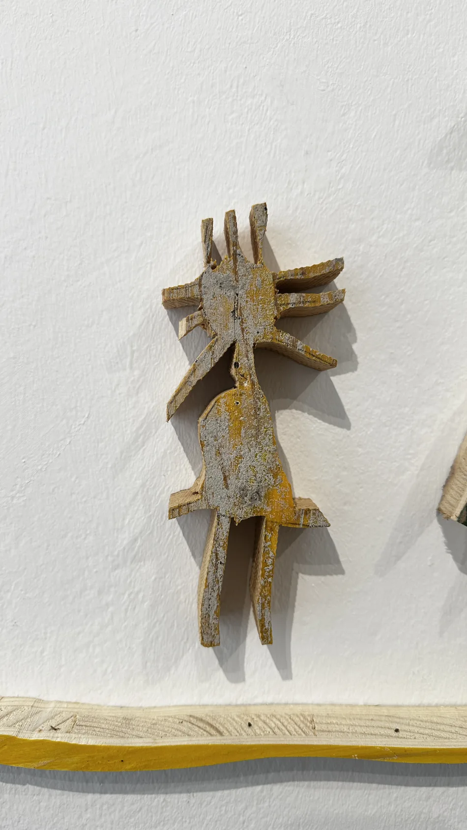 Detail of a small weathered grey and yellow formwork-timber figure on a gallery wall, Ernst Koslitsch, Cosmic Trigger – Respawn