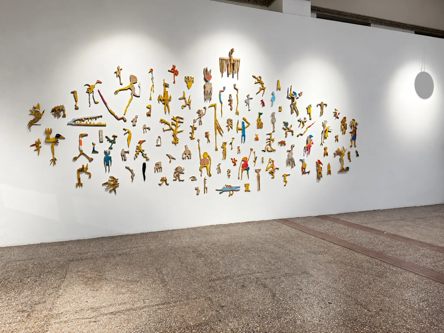Wide angle installation view of small painted wood cutout figures on a gallery wall, EX-SITU, Nationalmuseum Sarajevo, Ernst Koslitsch