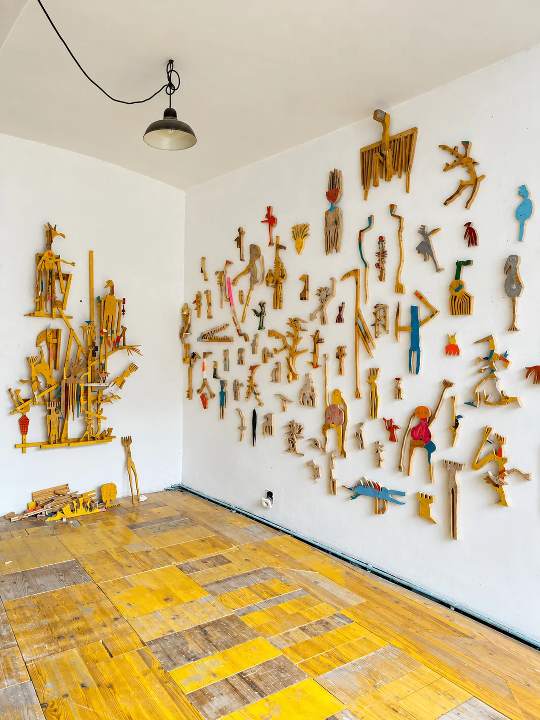 Studio corner with a wide wall installation of small painted wood cutout figures in progress, work for EX-SITU, Nationalmuseum Sarajevo, Ernst Koslitsch