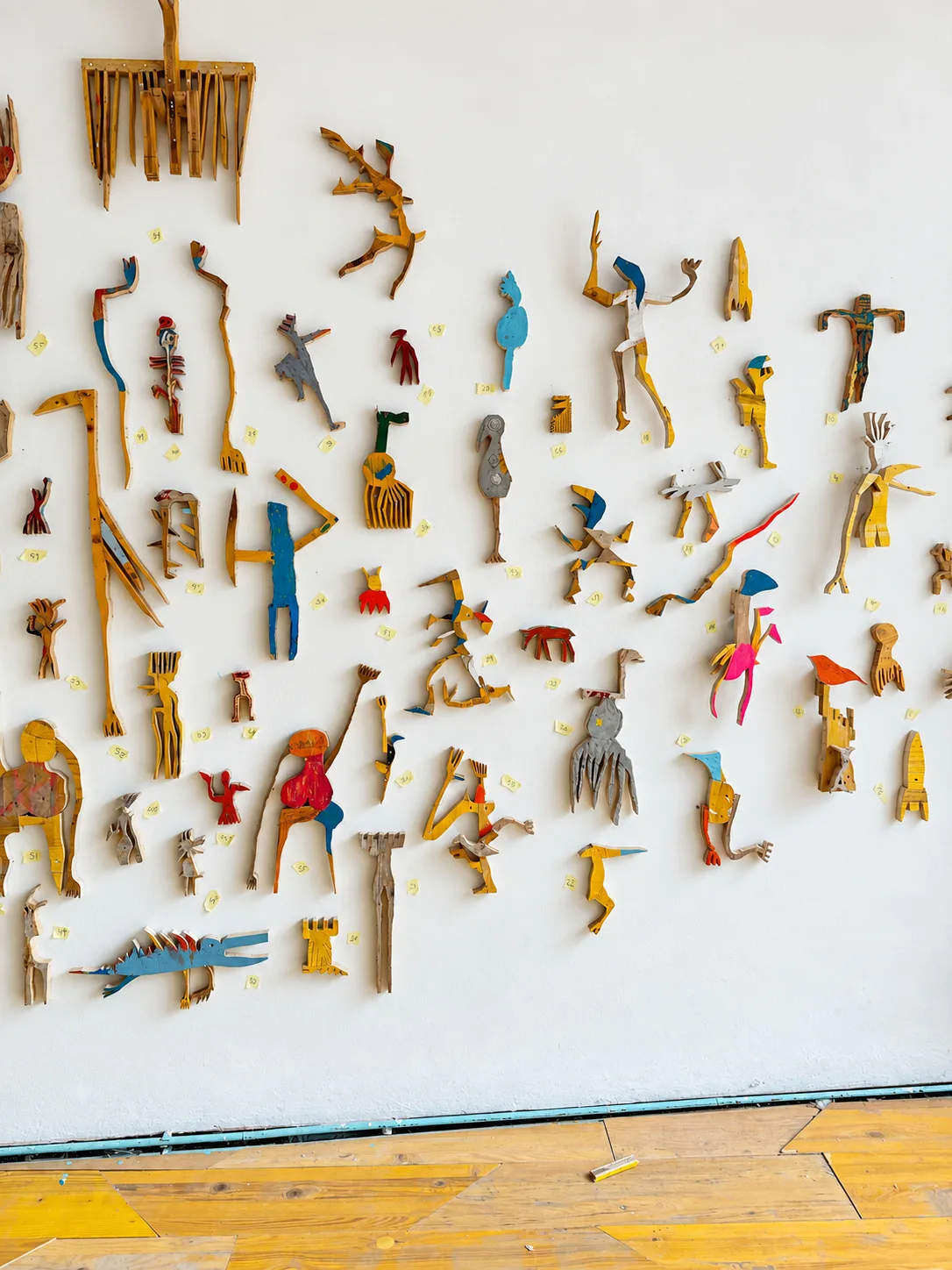 Studio wall covered with small painted wood cutout figures arranged with numbered tags, work in progress for EX-SITU, Ernst Koslitsch