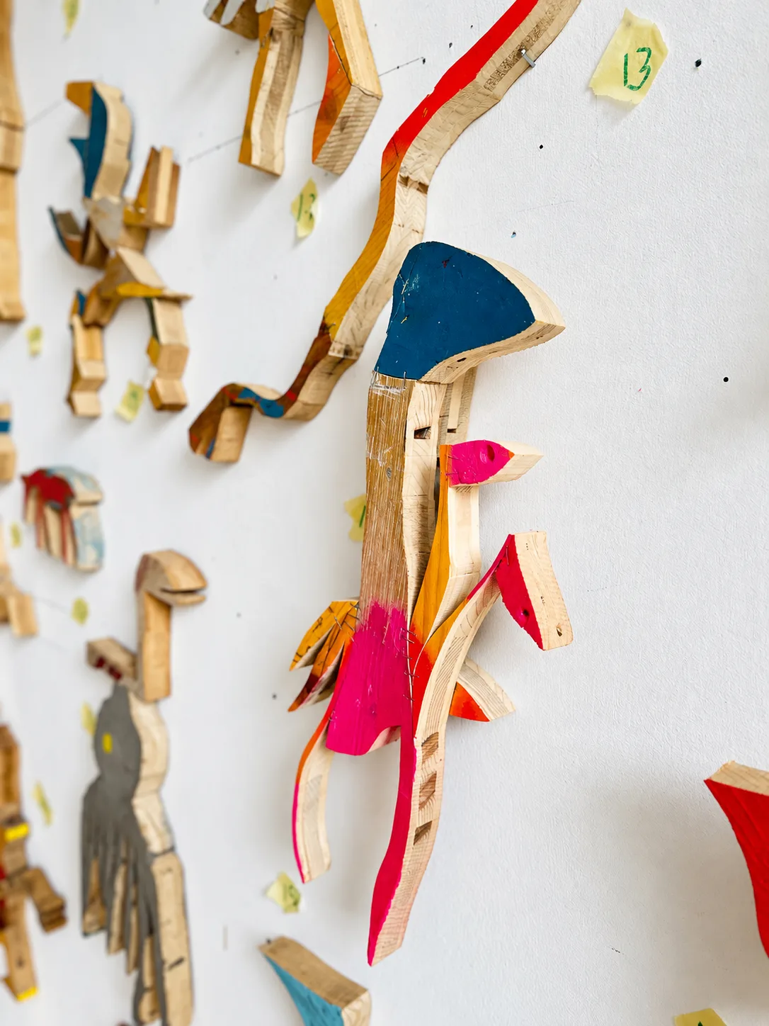 Close-up detail of painted wood cutout figures on a studio wall, numbered tags for arranging the installation, Ernst Koslitsch