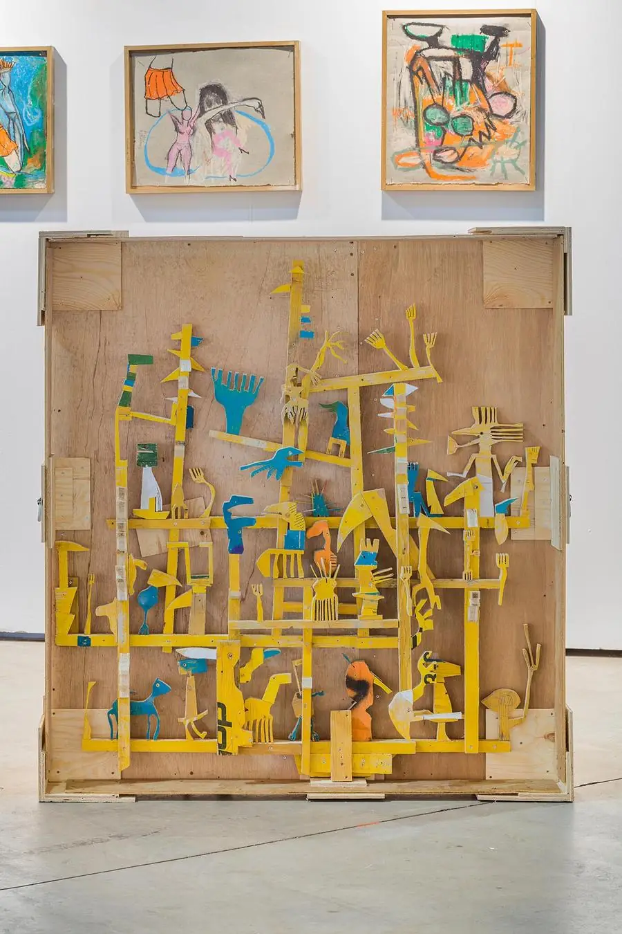 Yellow wood wall sculpture with paintings above, Spark Art Fair booth
